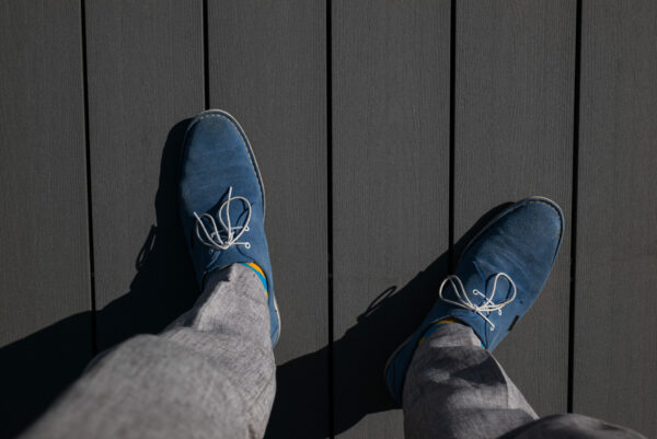 Miehen jalat harmaalla terassilla. Miehellä on harmaat siistit housut ja siniset kengät.