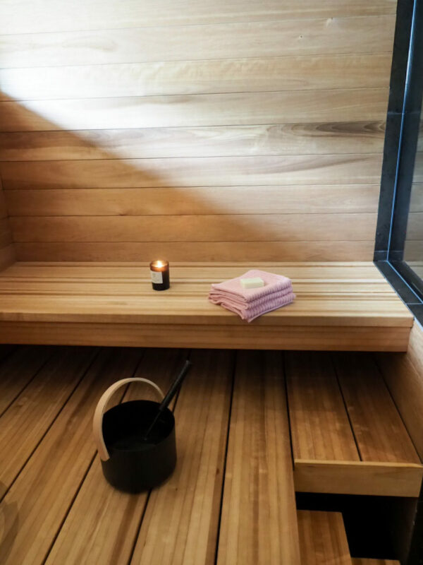 Kaunis lämpöhaapa sauna leveillä lauteilla. Lauteilla vaaleanpunaiset pyyhkeet ja kynttilä.