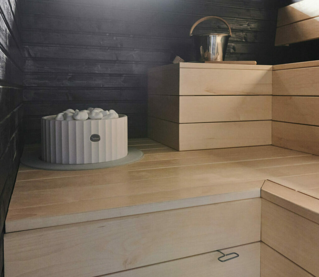 Musta sauna, jossa vaaleat haapalauteet ja valkoinen kiuas.
